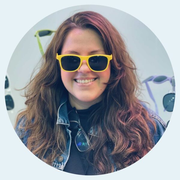 foto da Dra. Bárbara, mulher, com cabelos castanhos soltos, um óculos escuro amarelo e sorrindo.