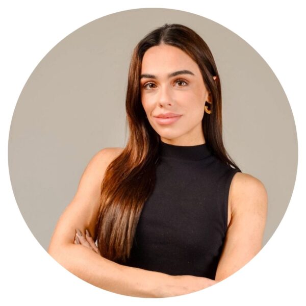 foto da Dra Paola, mulher de pele clara, cabelos longos, castanhos, de roupa preta e braços cruzados, com leve sorriso.