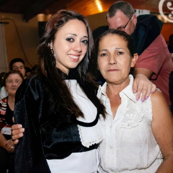 Bruna, mulher de cabelos castanhos e pele clara, abraçando uma senhora de roupa branca em sua formatura. Secretária Consultório Dr. Claudinei Kochinski