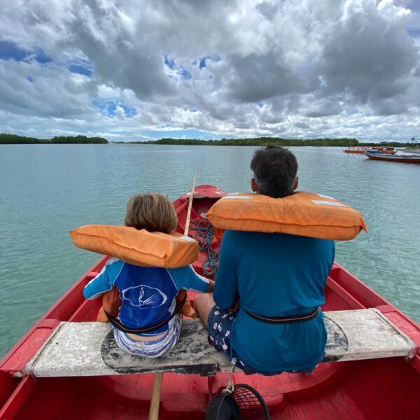 Dr. Claudinei Kochinski e seu filho de costas, em cima de um barco, estilo canoa, olhando pro horizonte no rio.