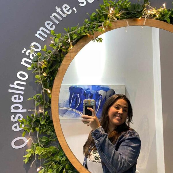 Mulher de cabelos pretos e um celular na mão tirando foto no espelho no consultório do Dr. Claudinei Kochinski